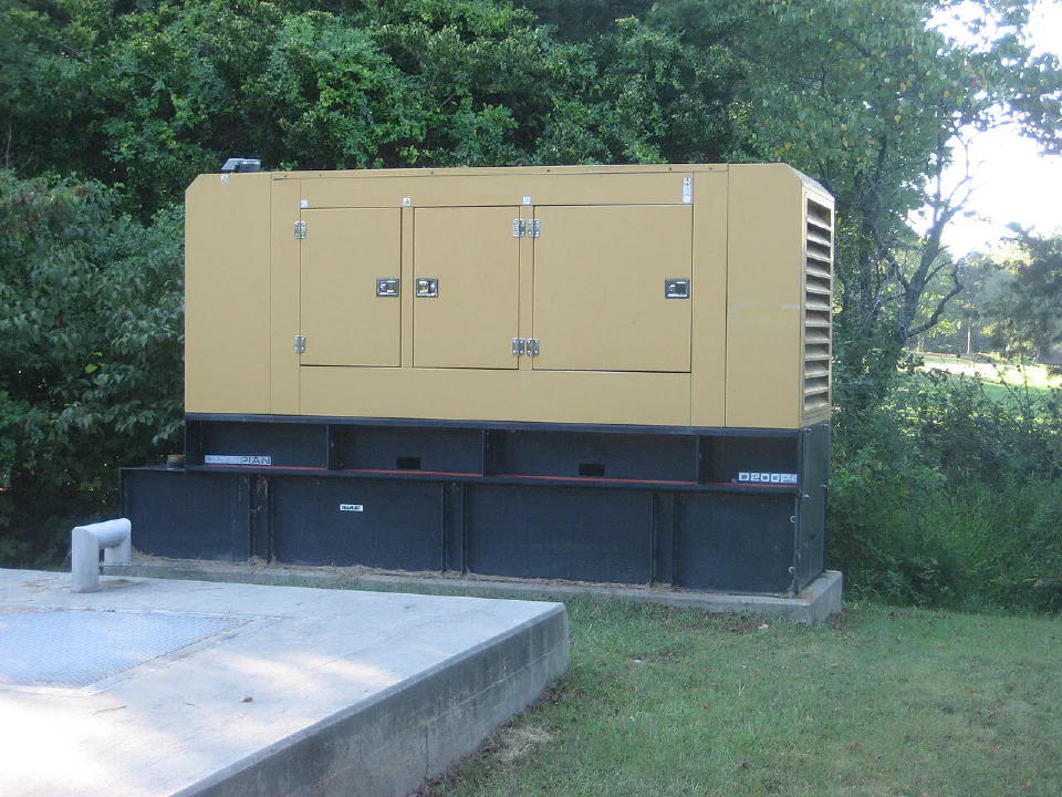 Enclosed yellow Olympian standby diesel generator on a concrete base outdoors beside trees